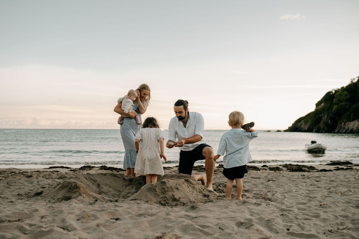 Family playing together on a scenic beach at sunset with cliffs in background.