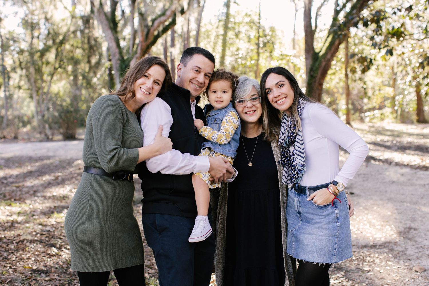 A group portrait of family members embracing outdoors among autumn trees.