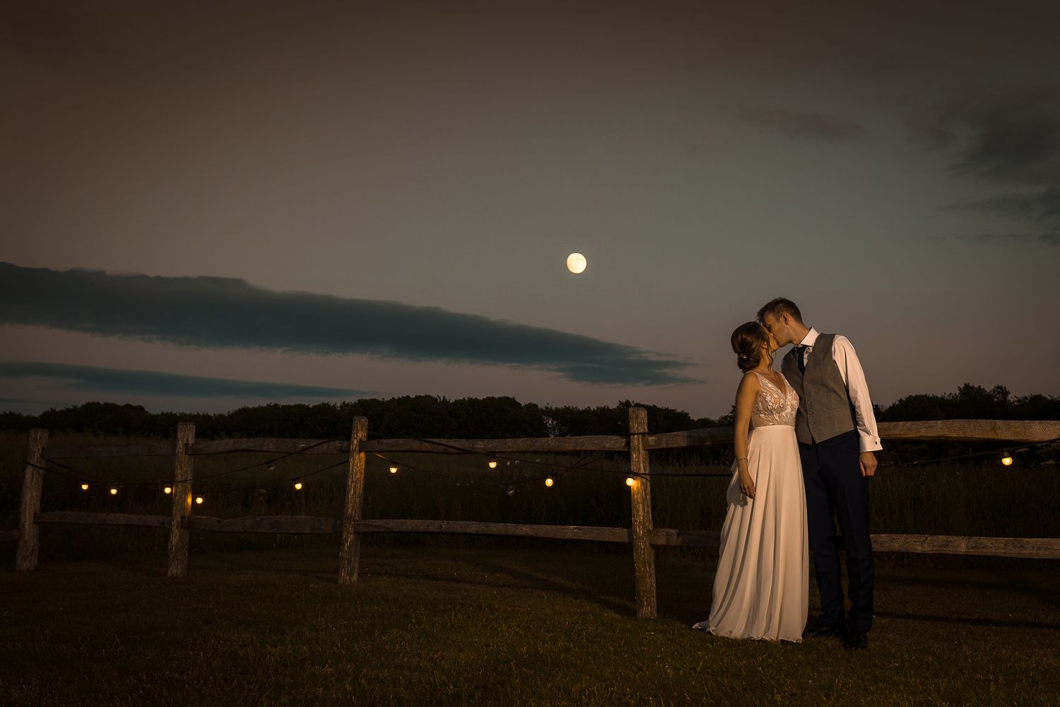 A romantic moonlit portrait of a couple by a wooden fence at night.