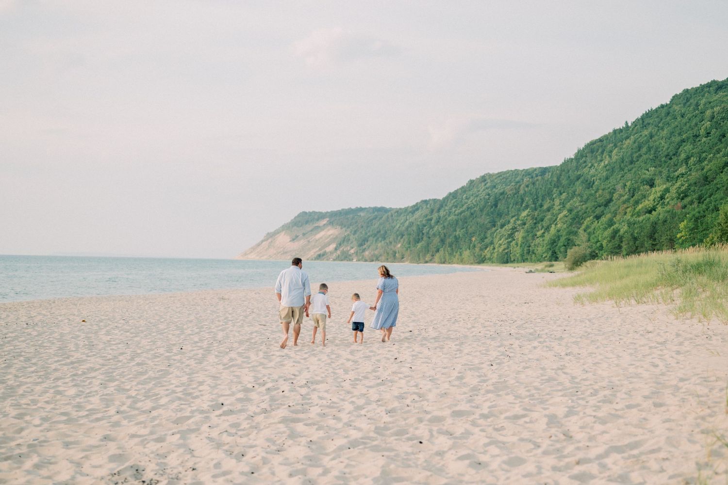 A family walking together on a pristine beach with forested cliffs in the background.