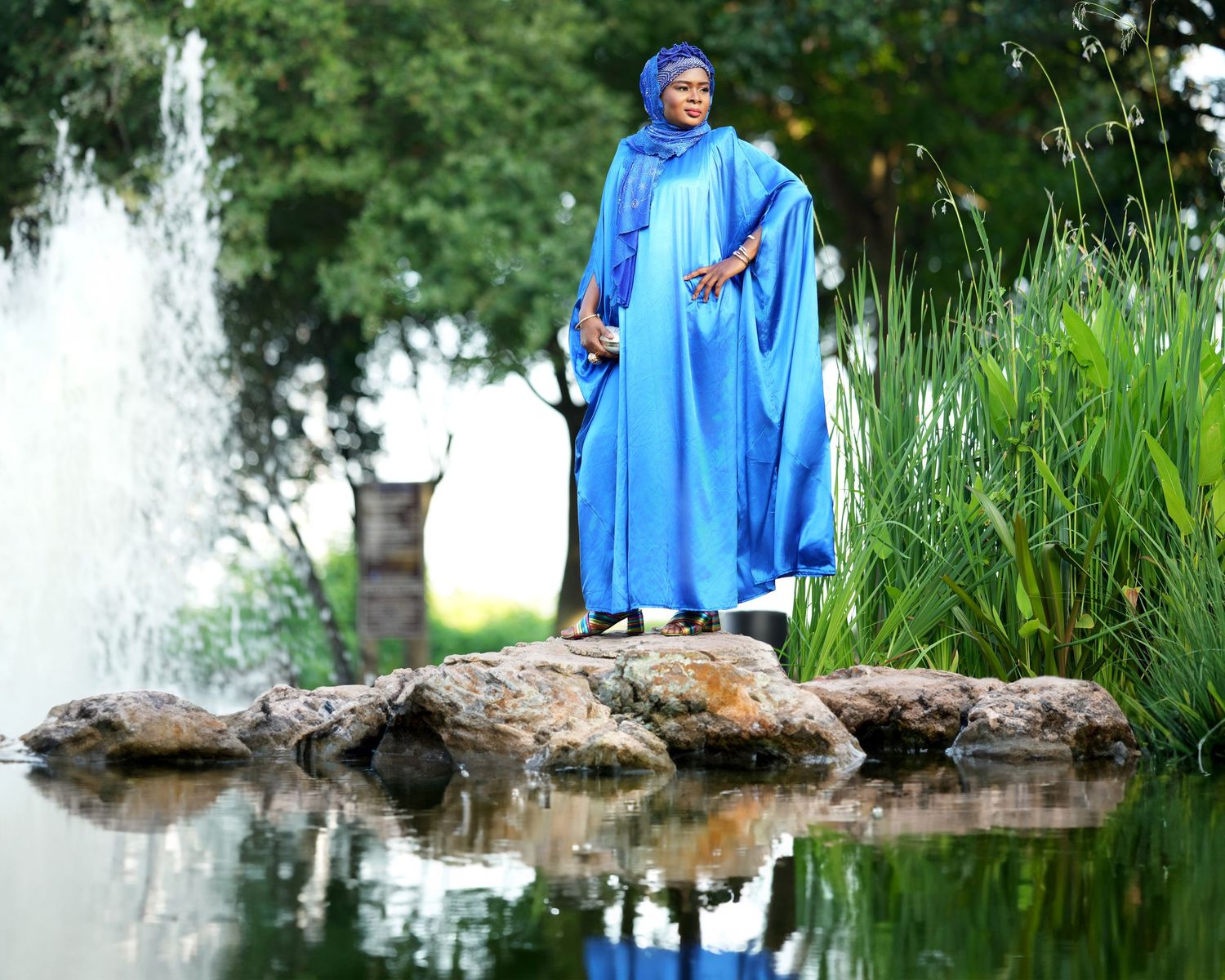A blue modest dress ensemble photographed near a fountain with water reflection.