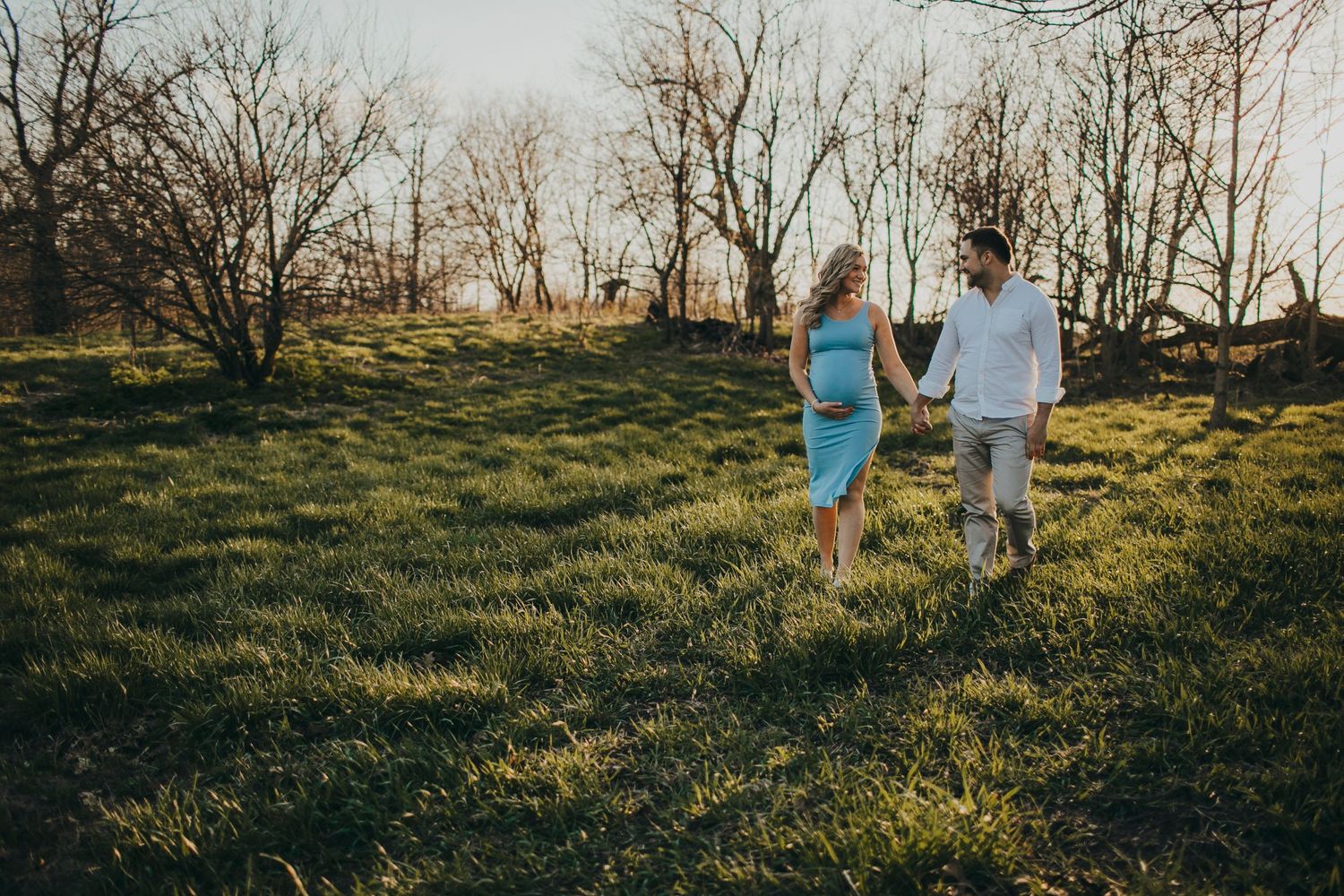 Couple walks through grassy field during golden hour sunset.