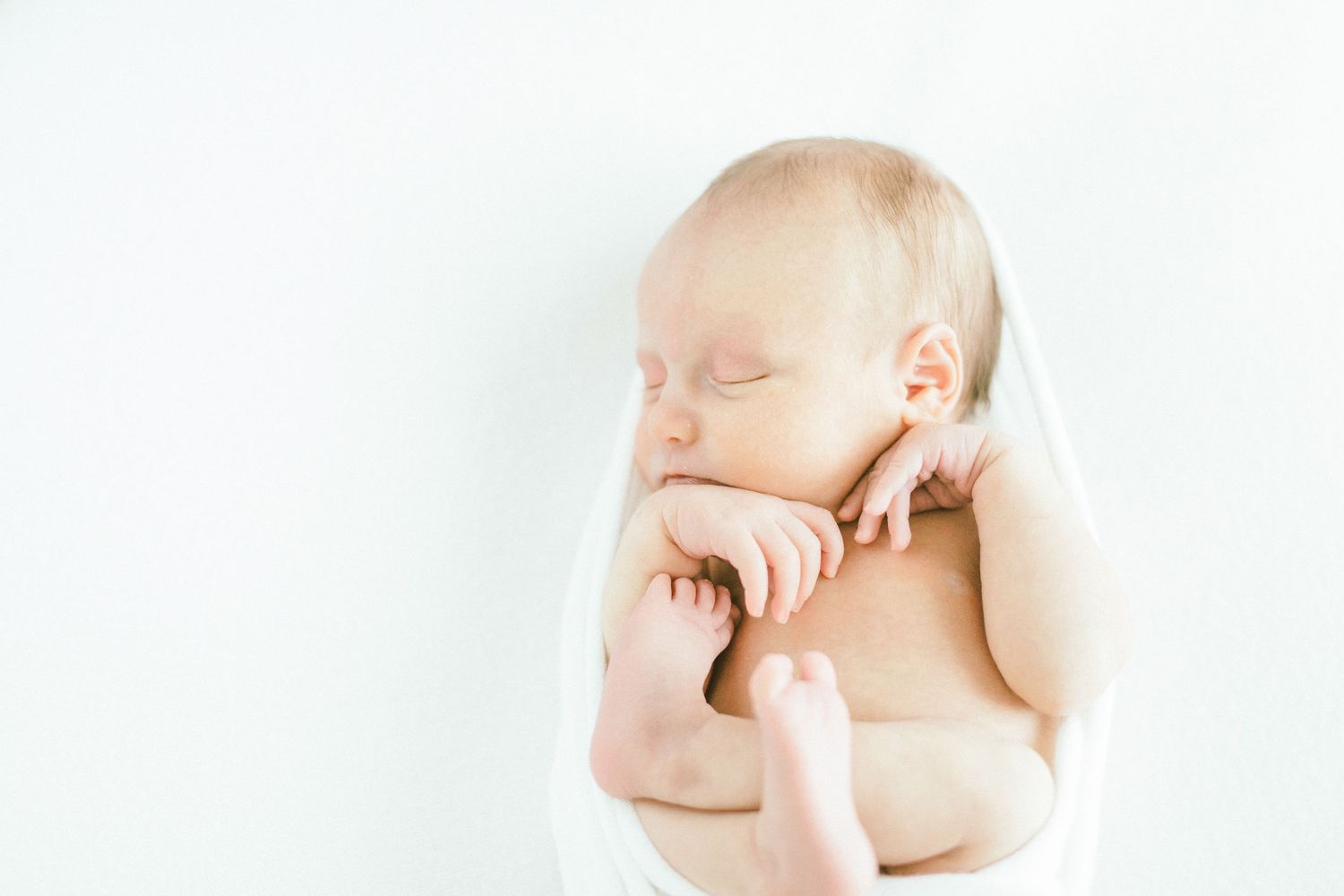 Peaceful sleeping newborn against white backdrop in natural light.