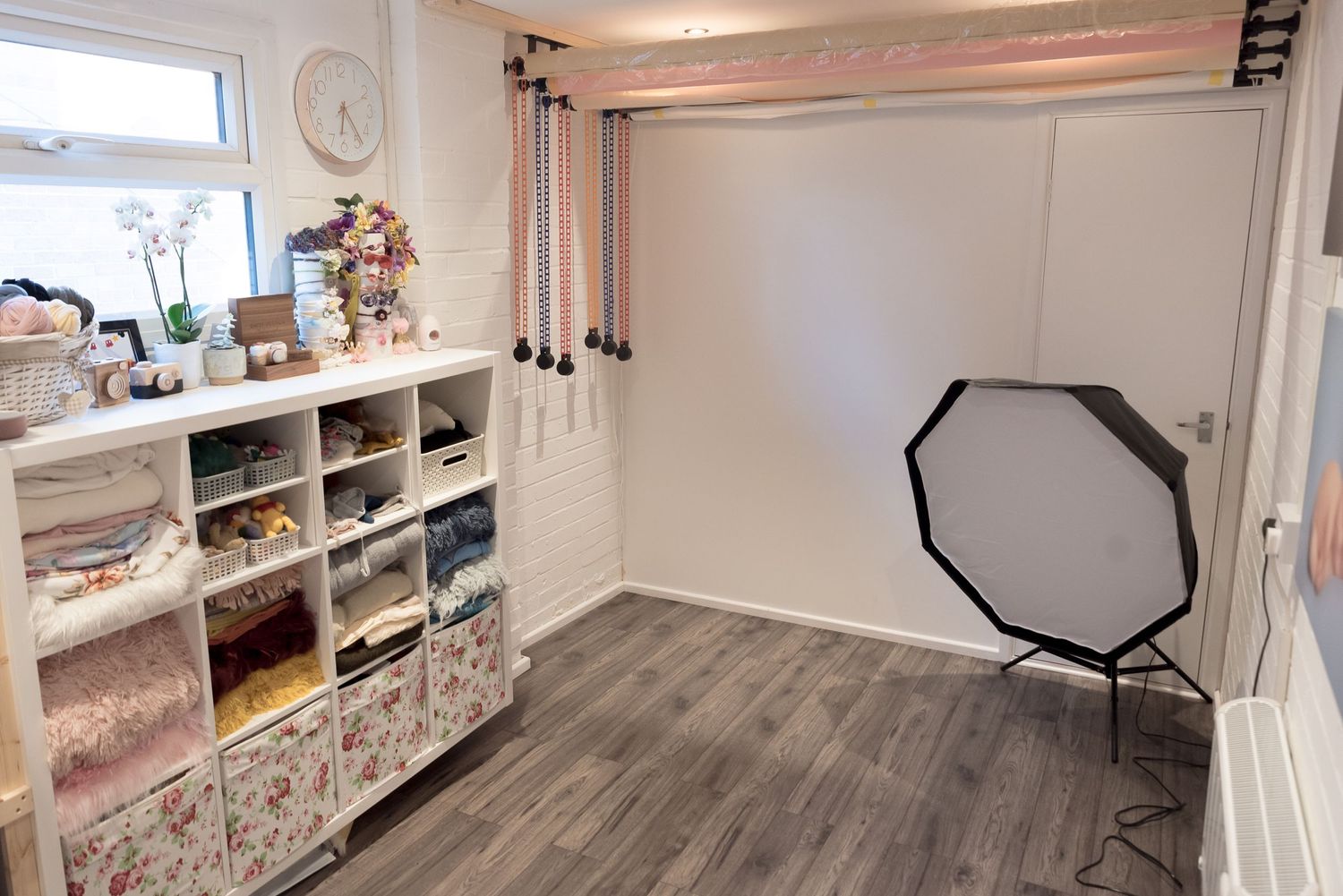 Photography studio room with white storage shelves and octagonal softbox light setup on grey flooring.
