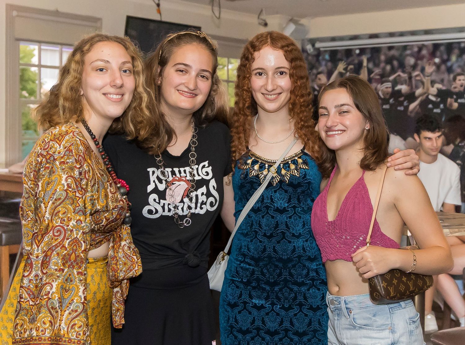 Four friends posing together at casual gathering with vintage crowd photo on wall.