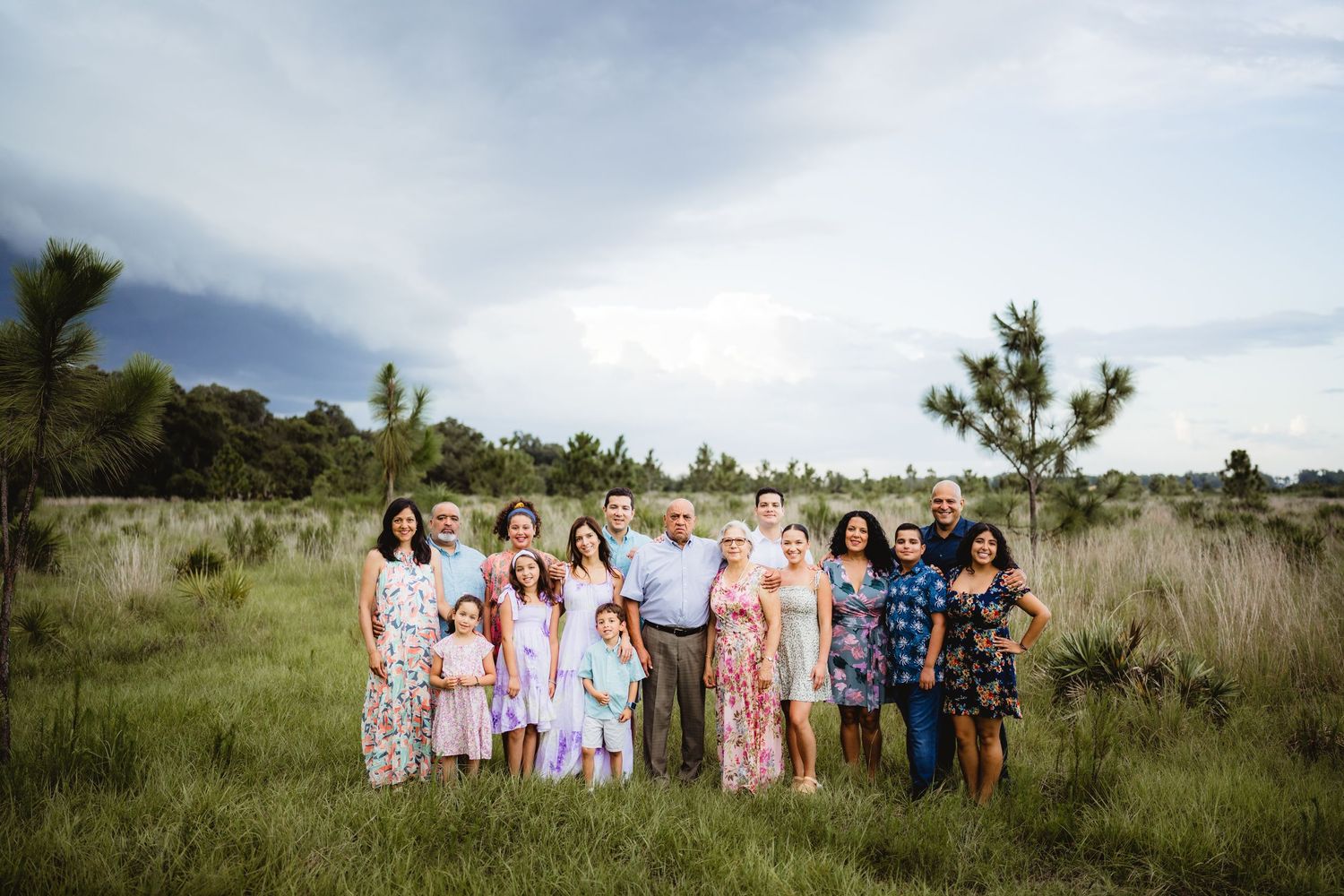 A large family group poses together in a grassy field under cloudy skies.