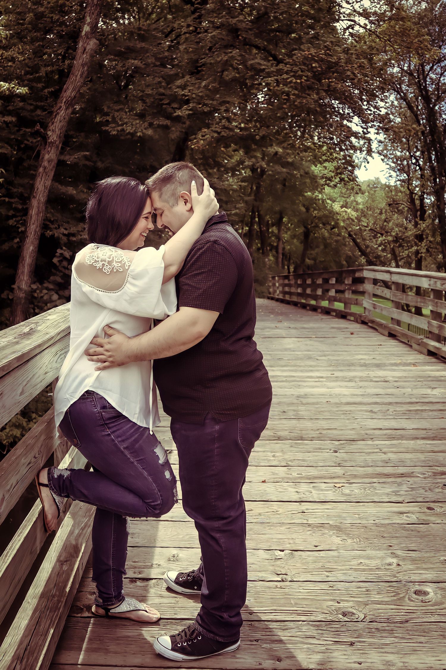 A romantic kiss between a couple on a wooden boardwalk surrounded by autumn trees.
