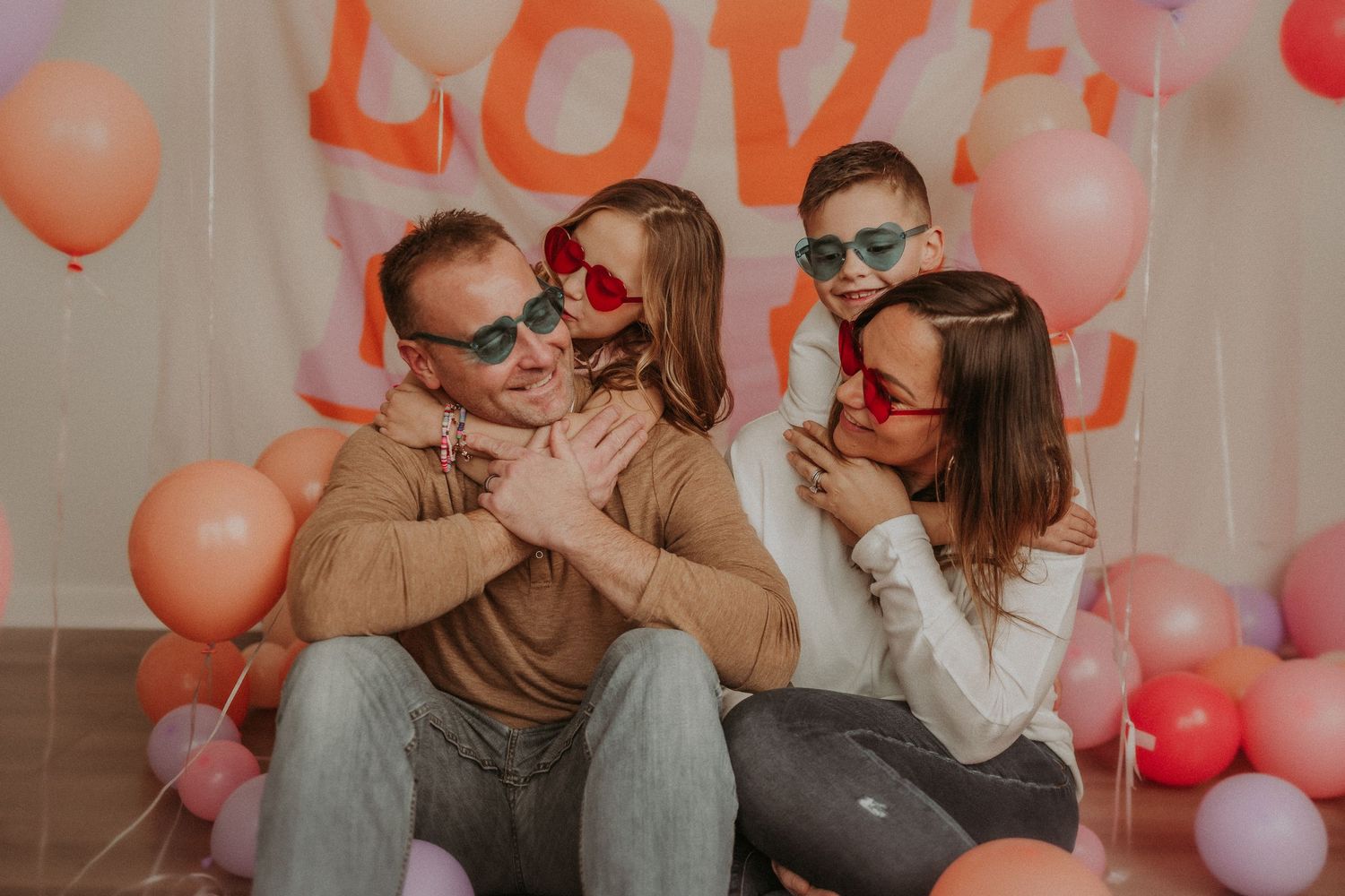 A fun family portrait with sunglasses against a pink backdrop with love text and balloons.