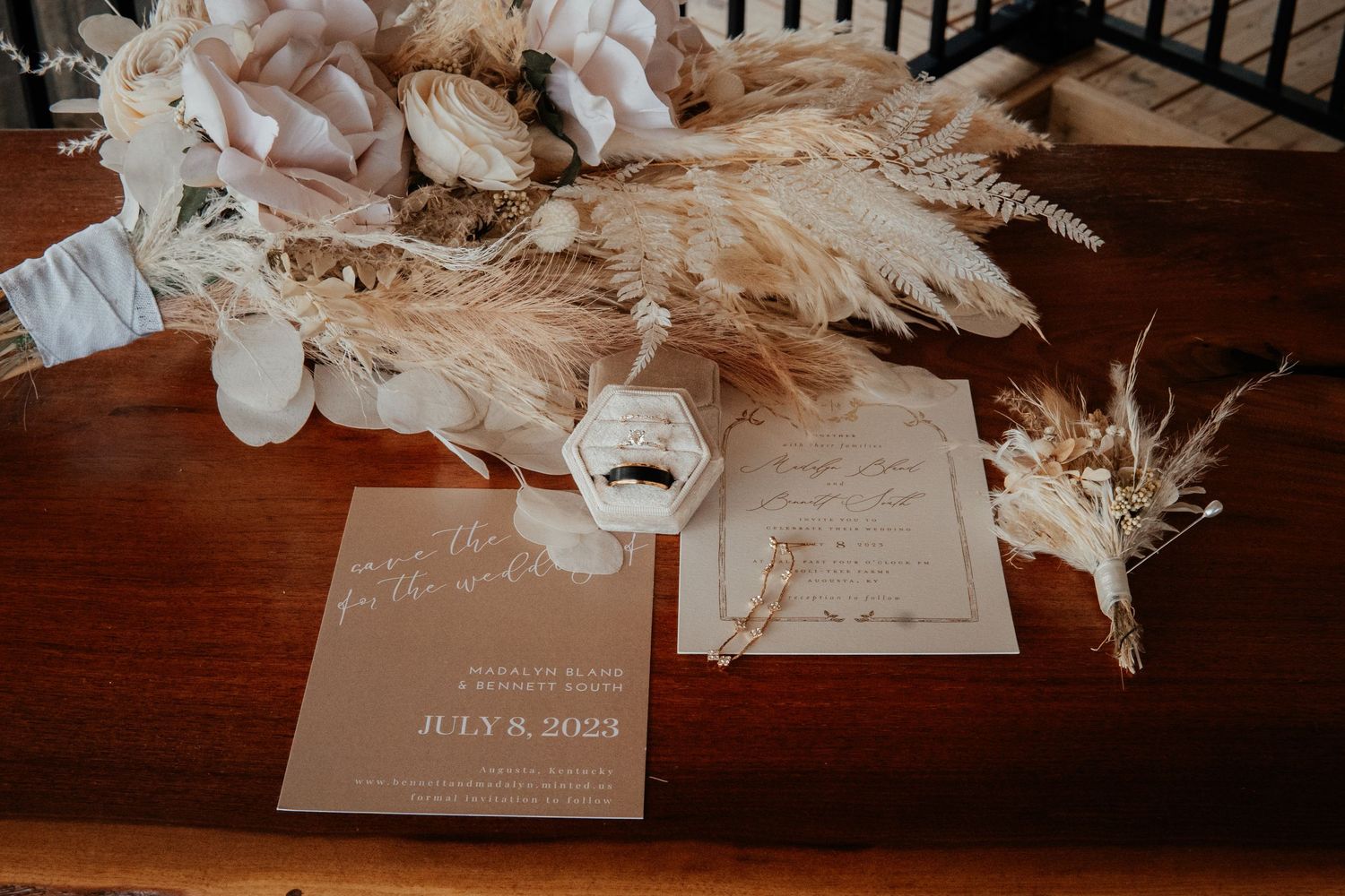 Wedding stationery and dried pampas grass arrangements on a wooden surface.