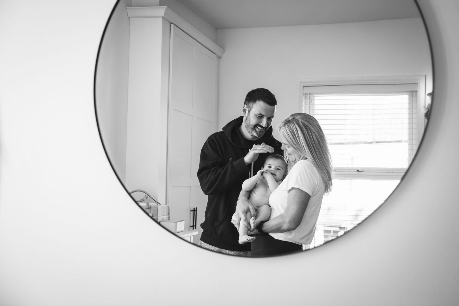 Black and white mirror reflection capturing family moment with infant.