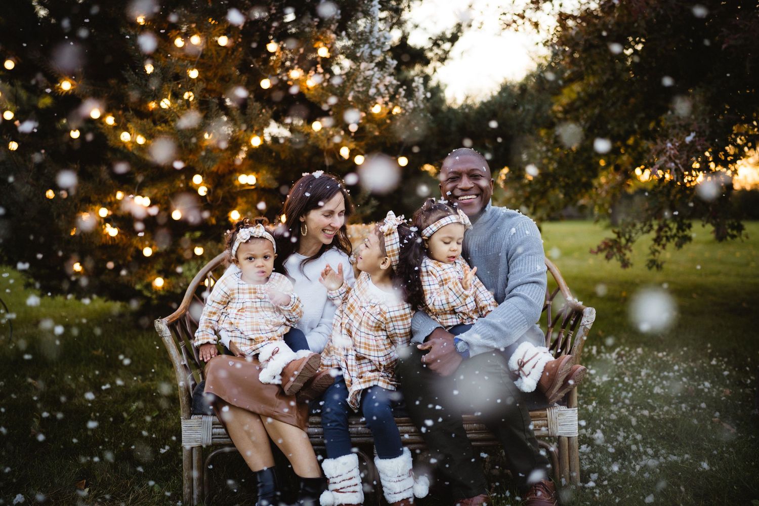 Family sitting together on outdoor bench with magical bokeh lights in background.