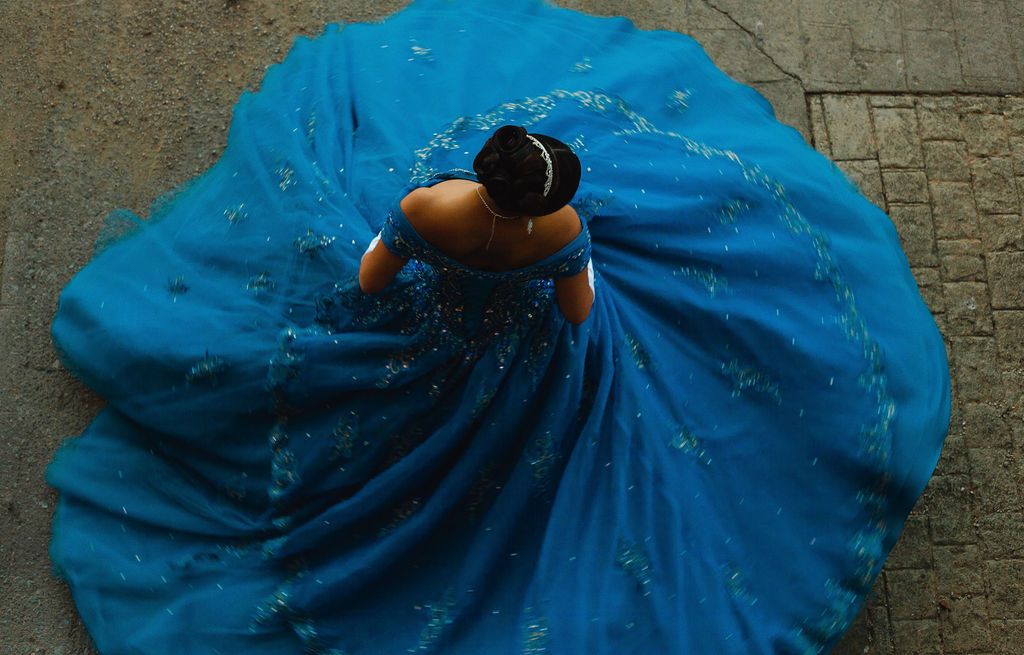A girl in her blue xv anos dress twirls around while Dallas, Texas's premier quince photographer snaps a shot from above