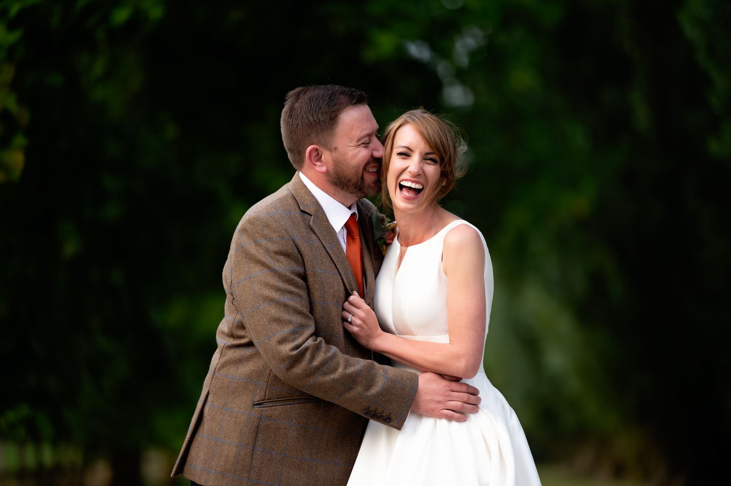Candid wedding couple laughing together in outdoor garden setting.