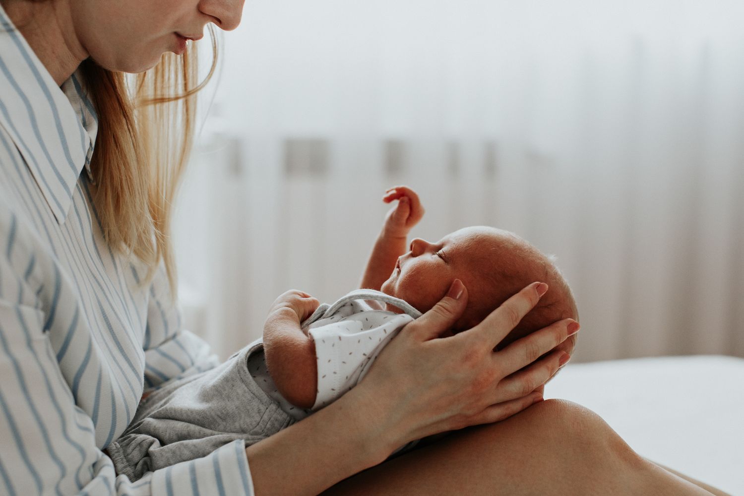 Blonde mother cradling sleeping newborn baby in gray onesie in her arms.