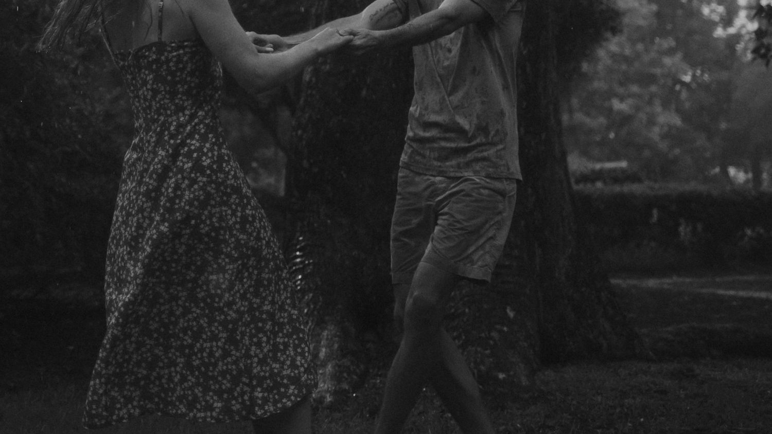 A couple dances together in a park setting captured in black and white photography.
