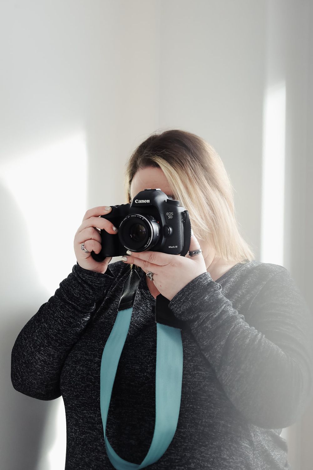 Photographer holding vintage camera against white wall with dramatic shadows.