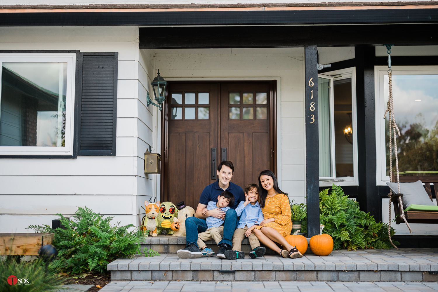 Family sitting on front porch steps decorated with autumn pumpkins.