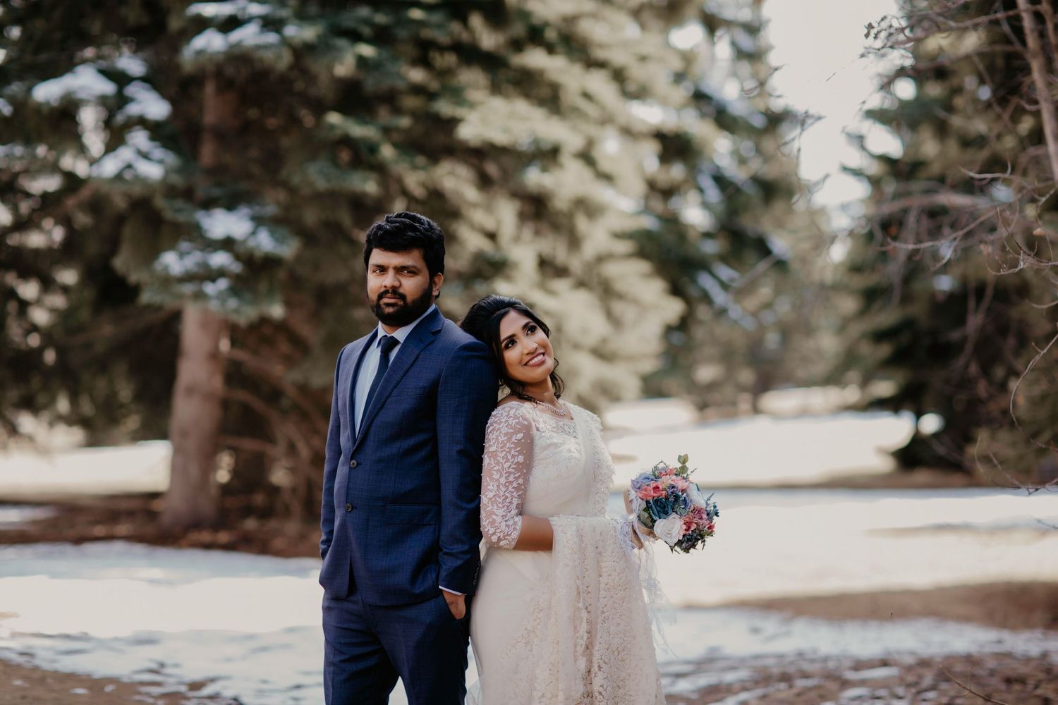 Newlywed couple stands together in snowy forest setting.