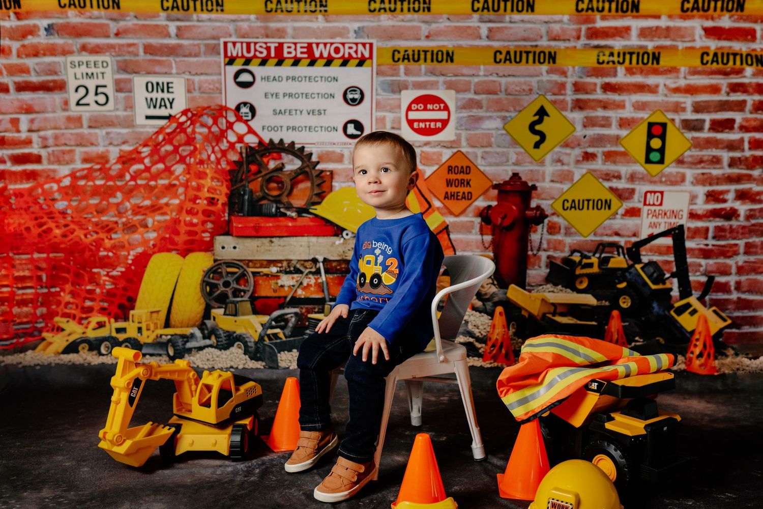 A construction themed photo with toy trucks and safety cones against a red brick wall.