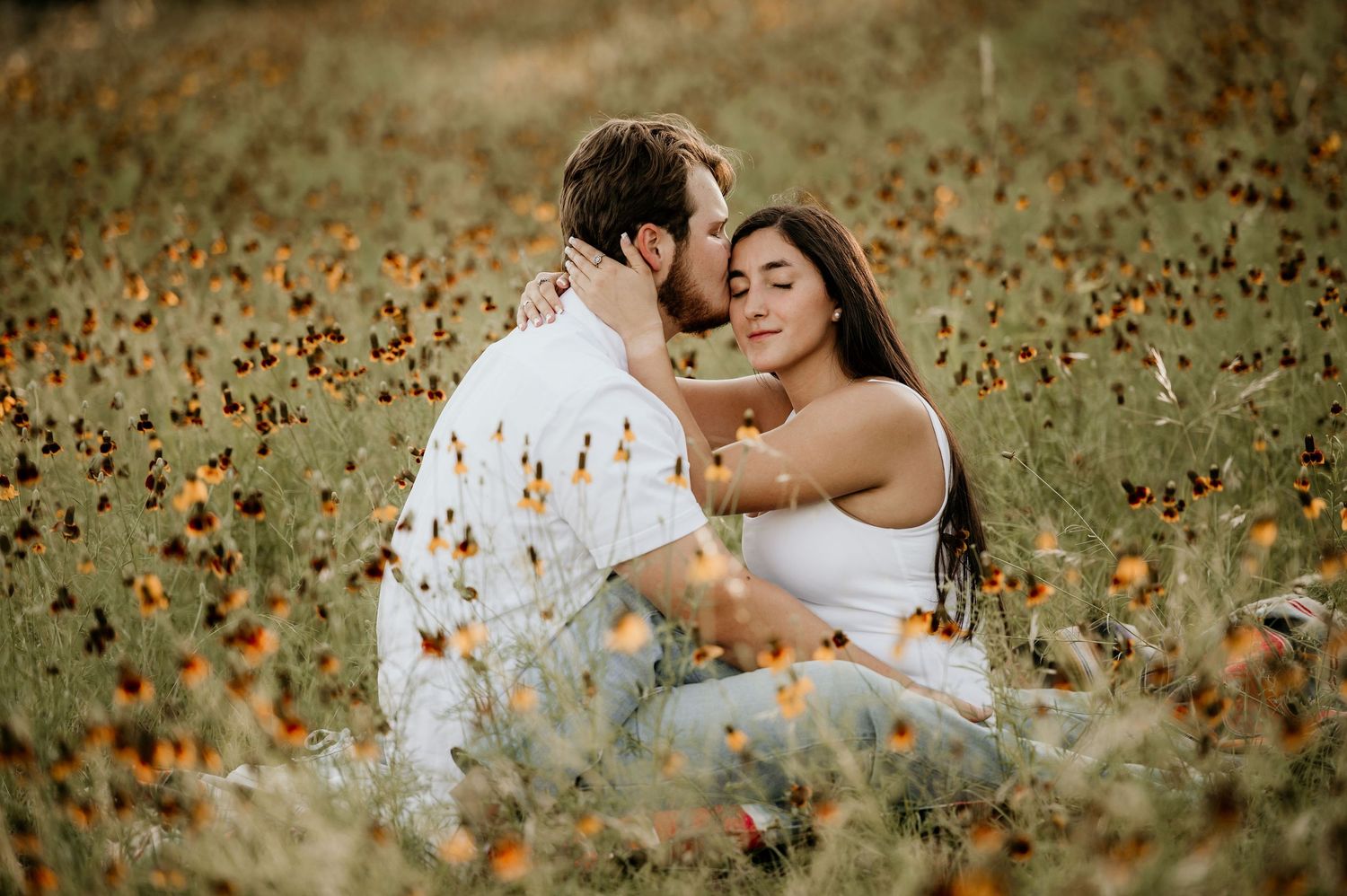 A romantic engagement photo of a couple embracing in a field of orange wildflowers.