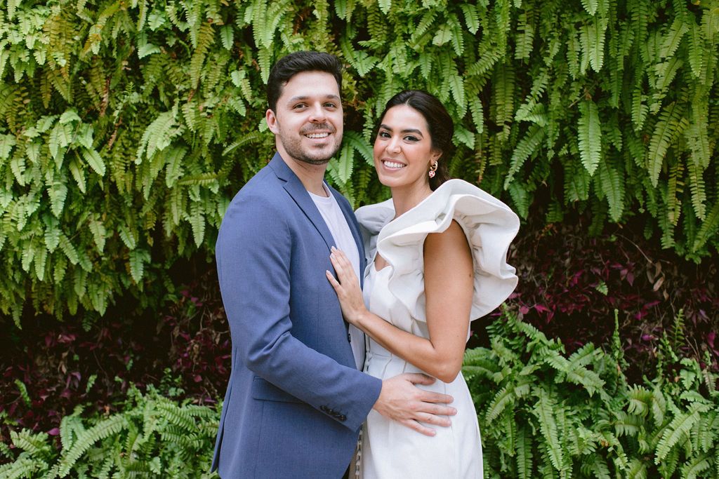 Wedding couple poses against leafy green backdrop in garden setting.