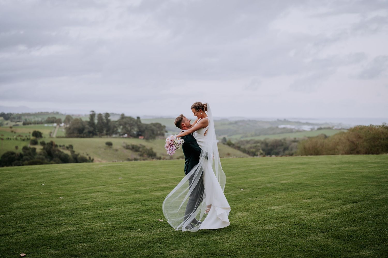 A wedding dress flows in the wind on rolling green hills during a countryside celebration.