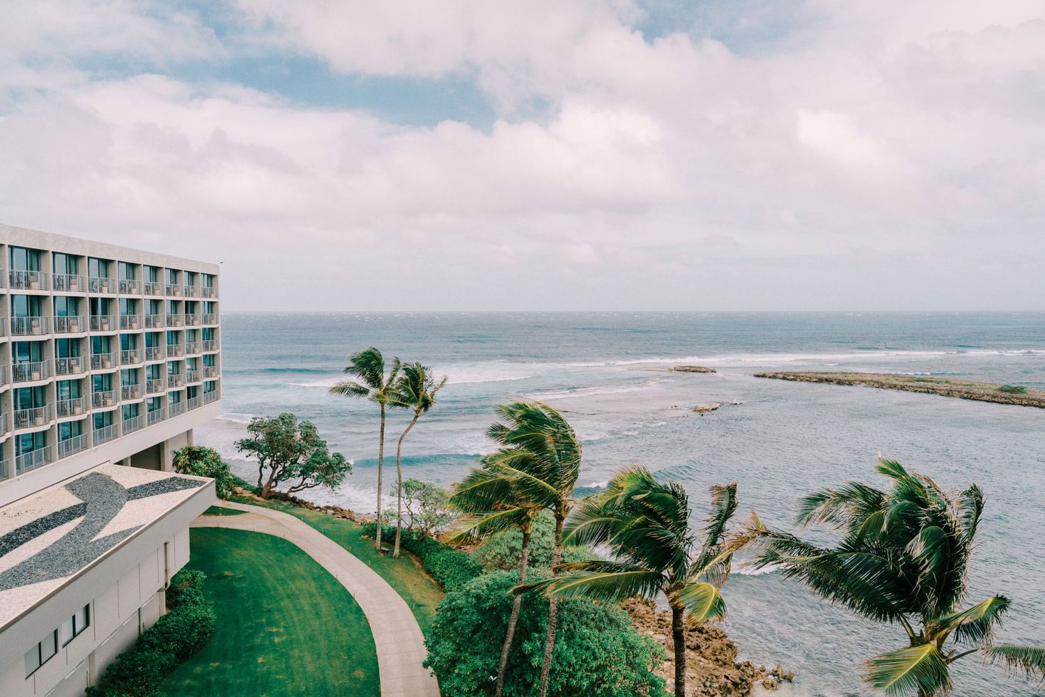 Beachfront hotel property with palm trees swaying in the wind on a cloudy day.