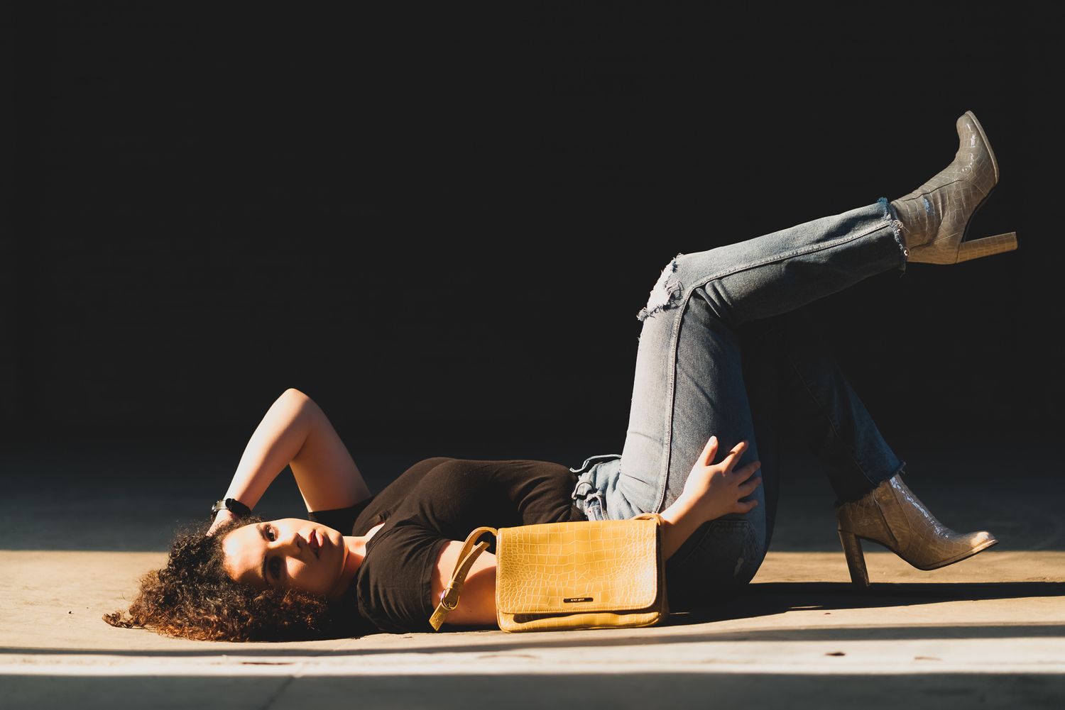 A person lies on wooden flooring next to a vintage suitcase in dramatic lighting.