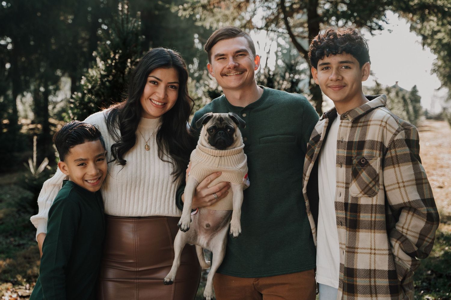 Family portrait outdoors with a pug dog against a natural background.
