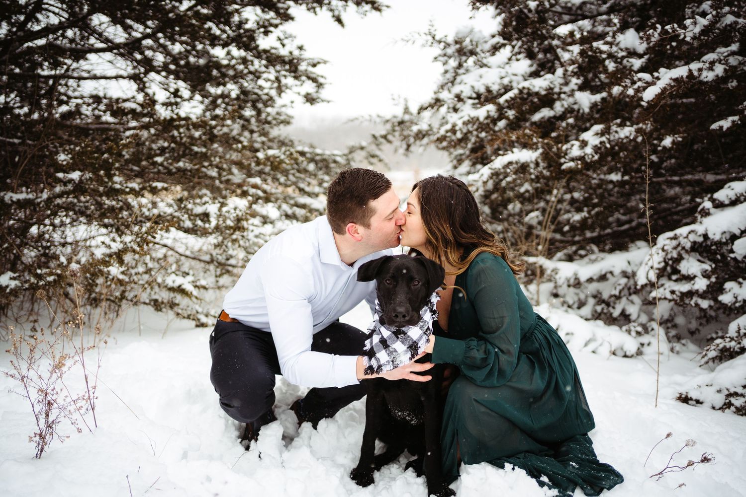A couple shares a tender moment with their dog during a snowy winter photoshoot.