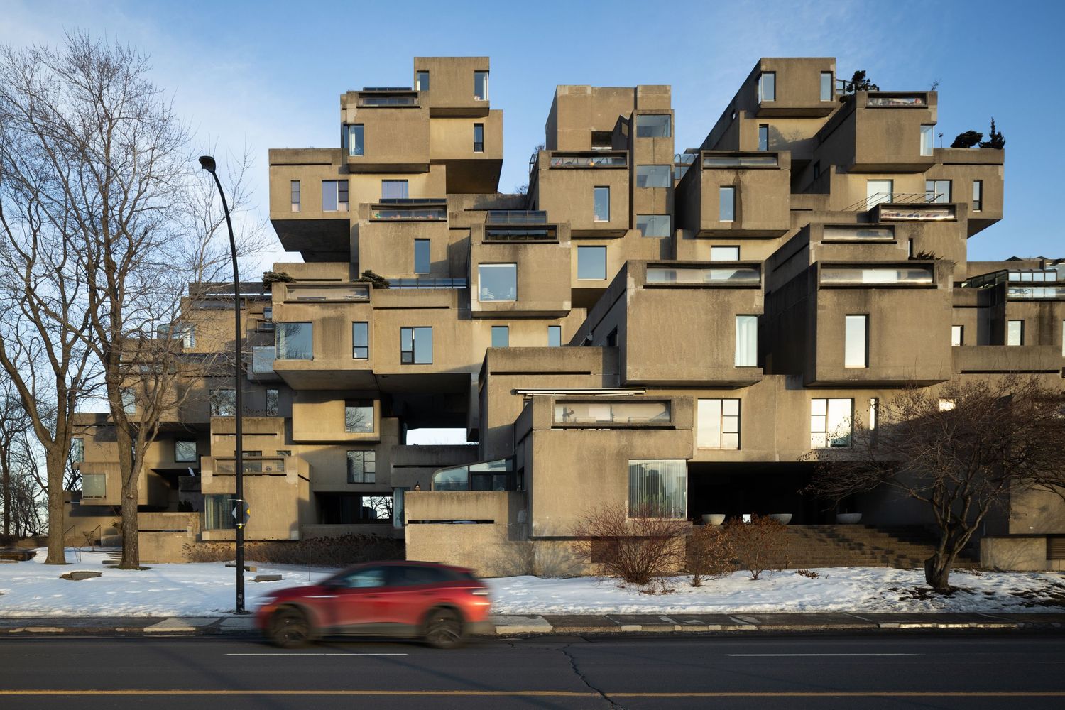 Brutalist apartment complex Habitat 67 in Montreal with stacked cubic modules and a red car passing by.