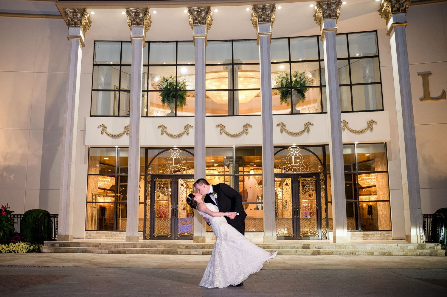 Bride and groom sharing a romantic dip kiss in front of the wedding venue