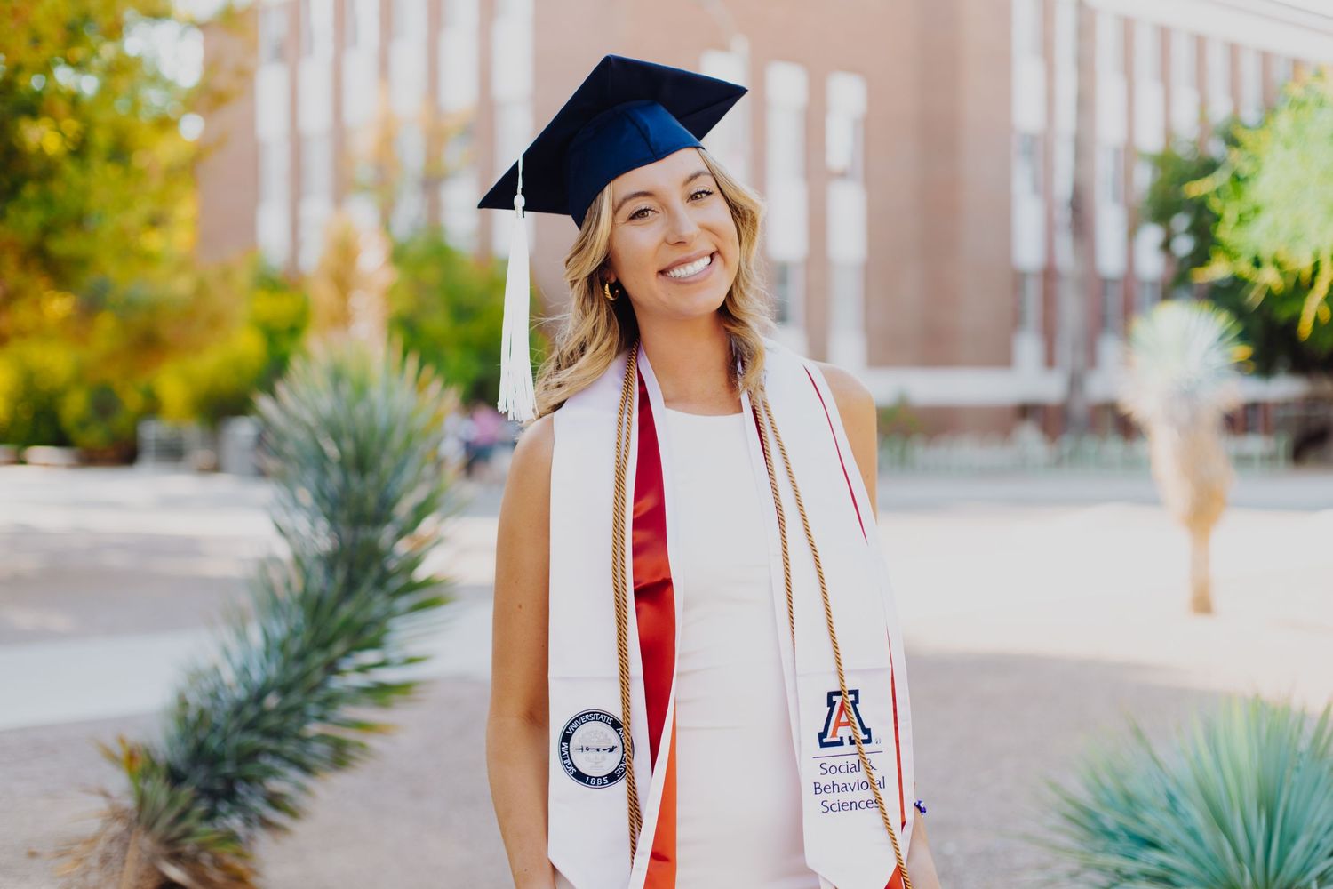 Graduation photo series in front of brick university building with desert landscaping.