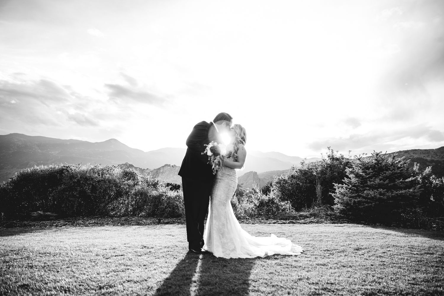 Black and white silhouette of wedding couple embracing on hilltop with mountain vista.
