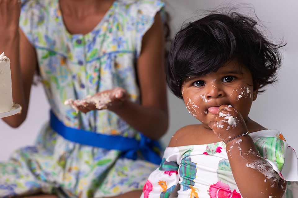 Smiling child in floral dress with cake frosting on face during birthday celebration.