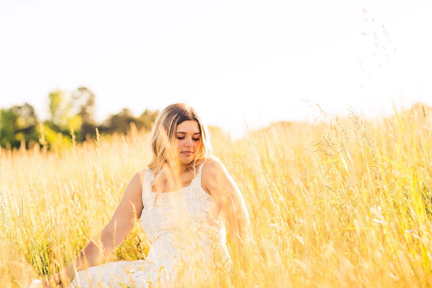 Woman in white dress walking through tall golden wheat field at sunset.