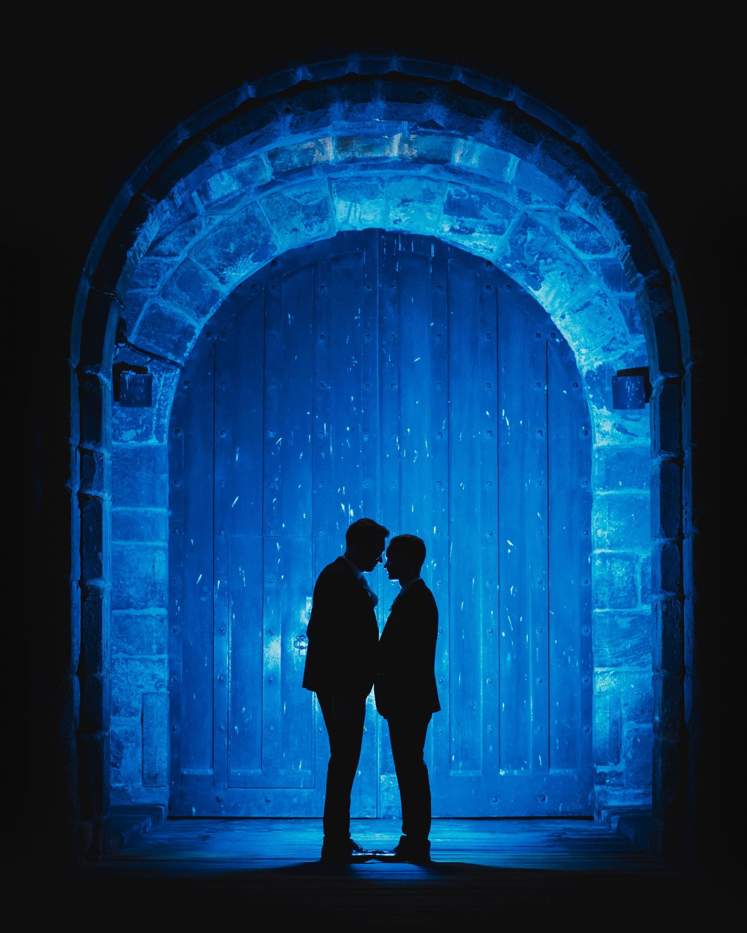 Two silhouettes share an intimate moment under a blue-lit stone archway.
