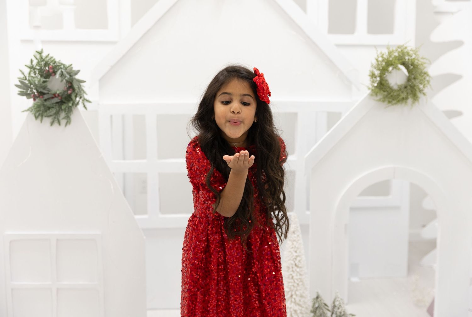 A festive scene shows a sparkly red dress and two decorative wreaths on a white background.