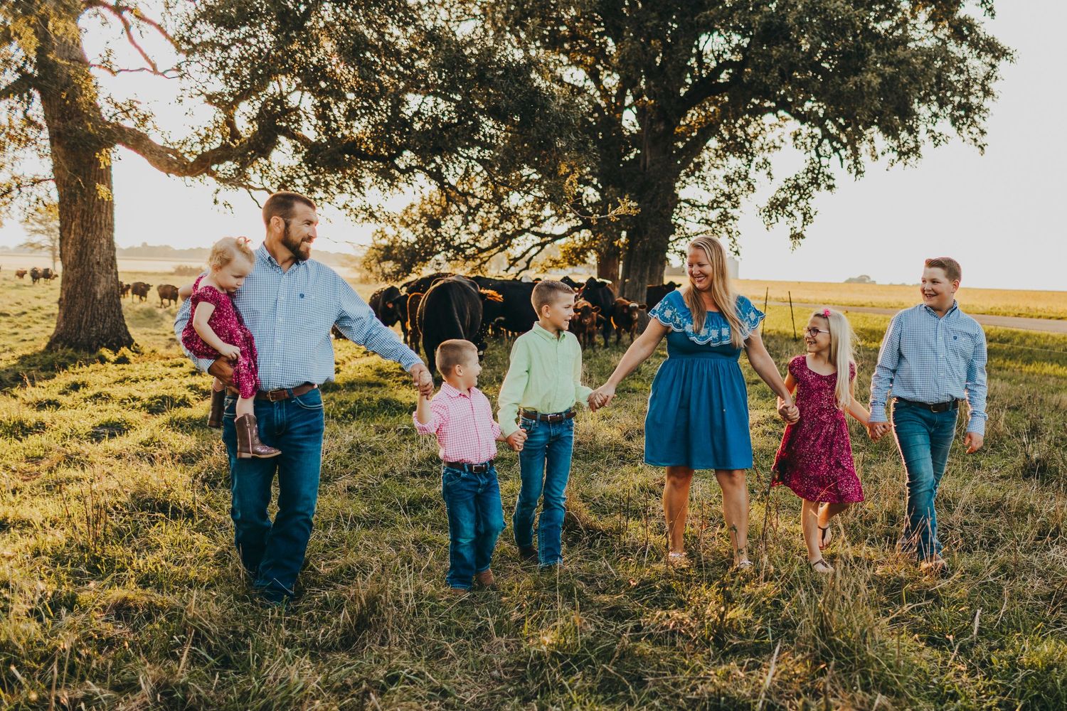 Family holding hands while walking together on grassy hilltop during golden hour.