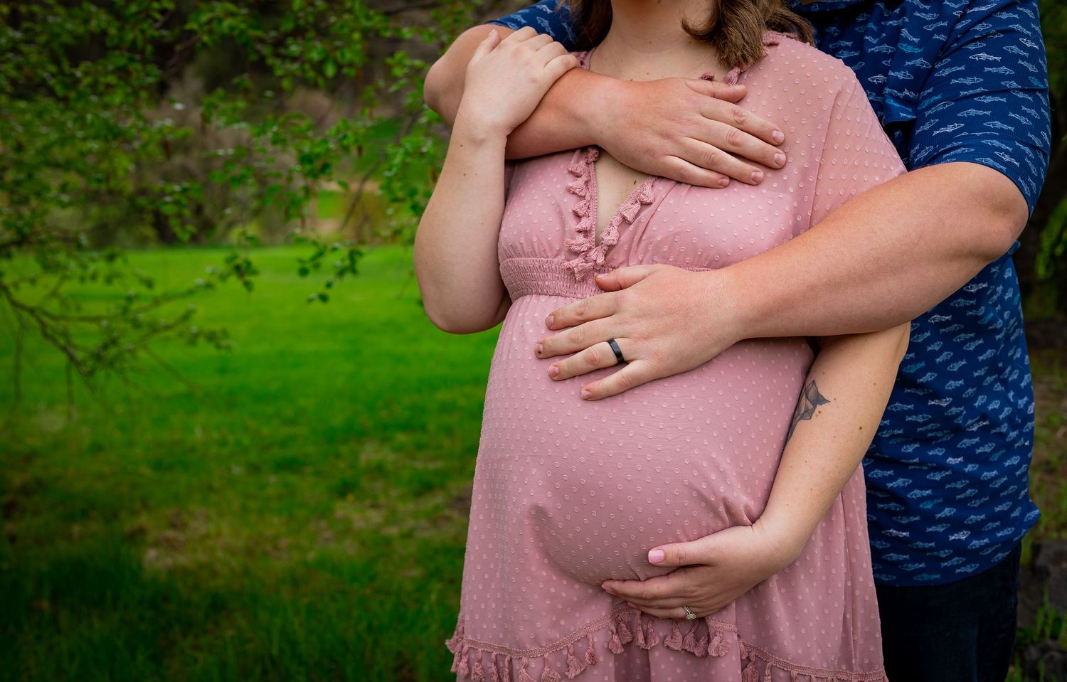 Maternity photo showing couple embracing with hands on pregnant belly in pink dress.