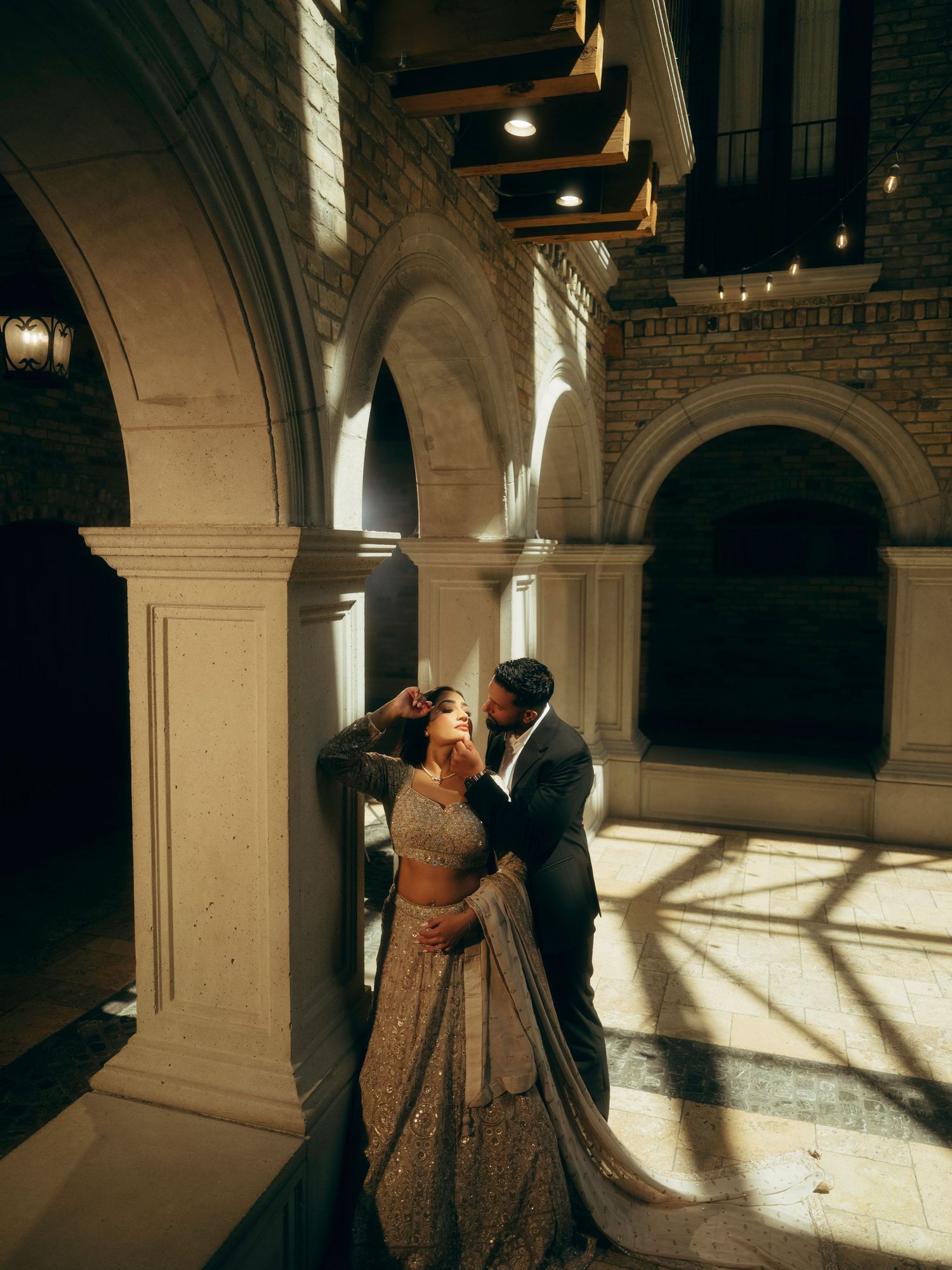 A couple in formal attire dances intimately in a sunlit stone archway corridor.