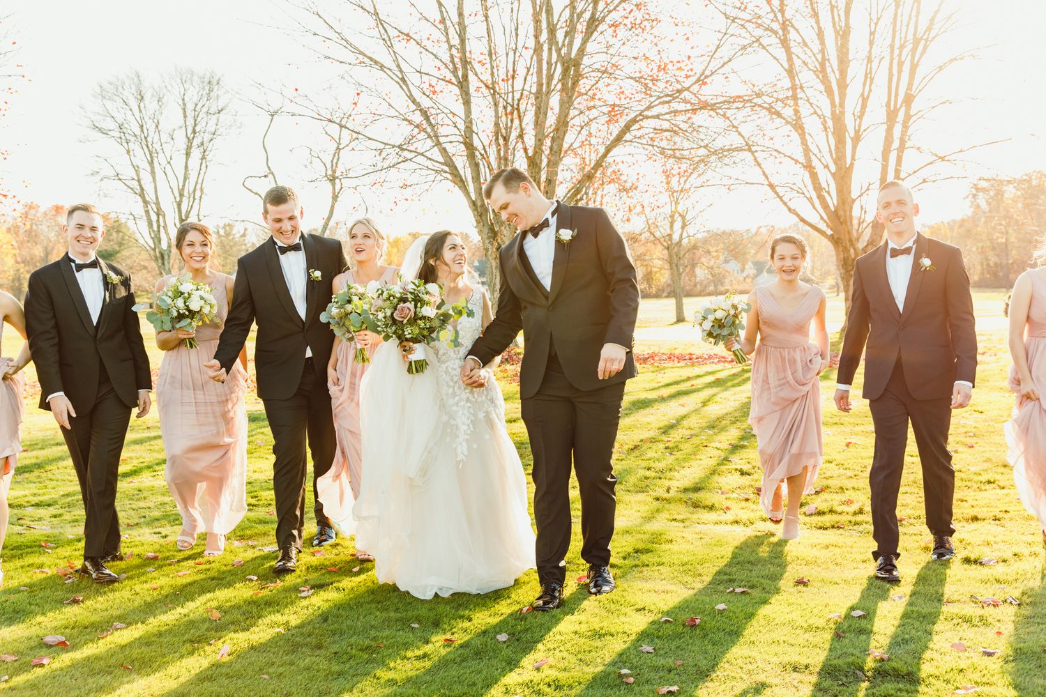 Wedding party poses together on grassy hill during sunset with long shadows.