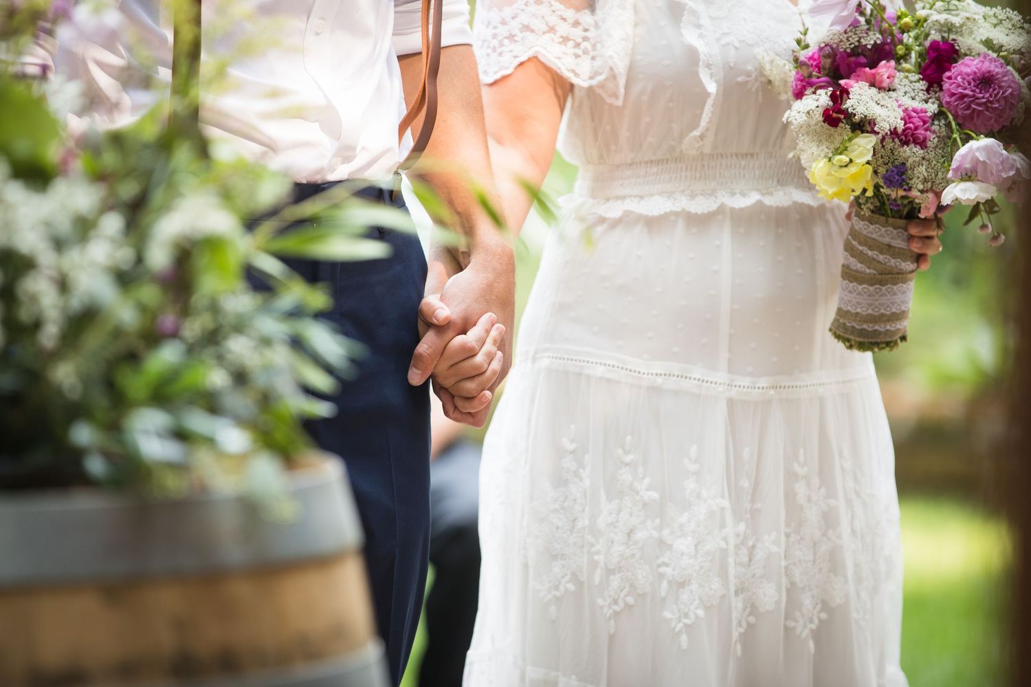 Close-up of a lace wedding dress and bouquet details in a garden setting.