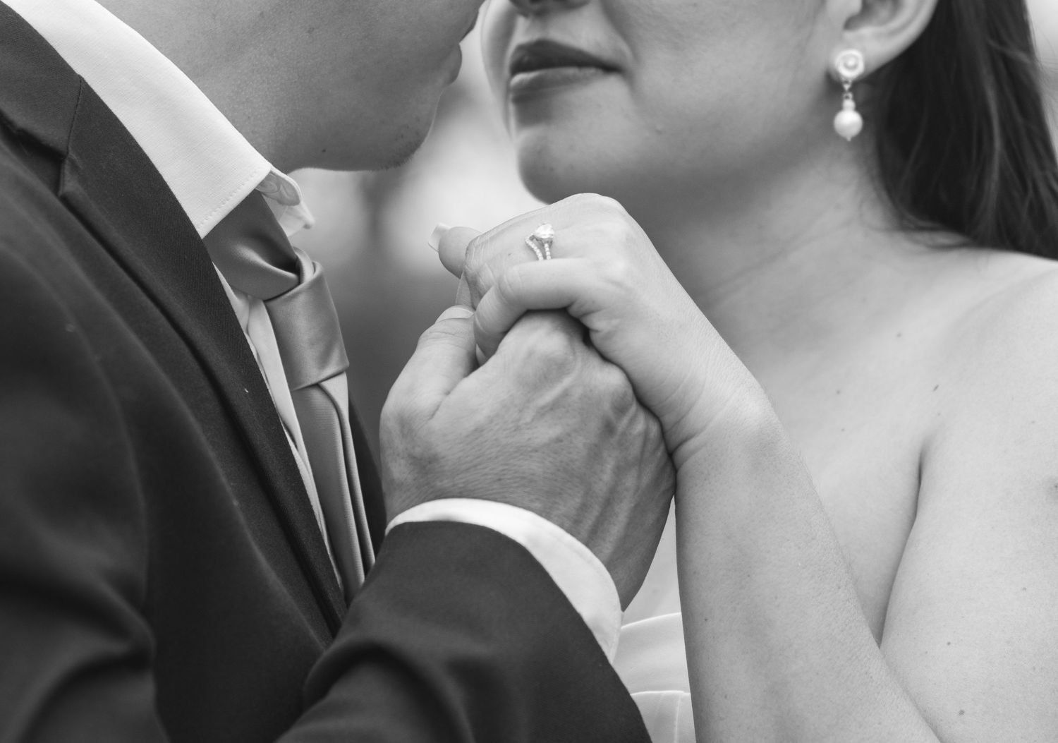 Close-up black and white photo of hands with wedding rings in an intimate moment.