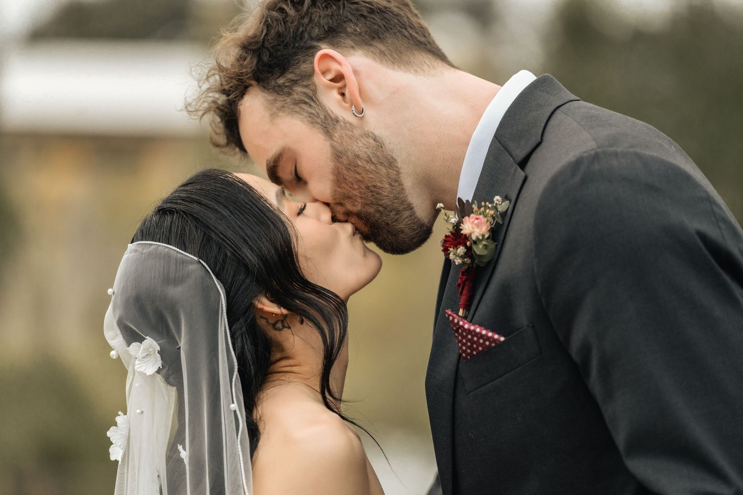 A bride and groom share a romantic kiss on their wedding day, with the bride wearing a veil and groom in a dark suit.