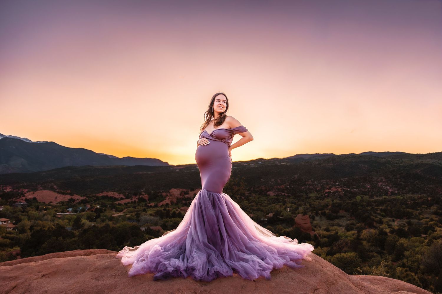 A person in a flowing lavender gown poses dramatically against a desert mountain landscape at sunset. Garden of the Gods, Colorado Springs