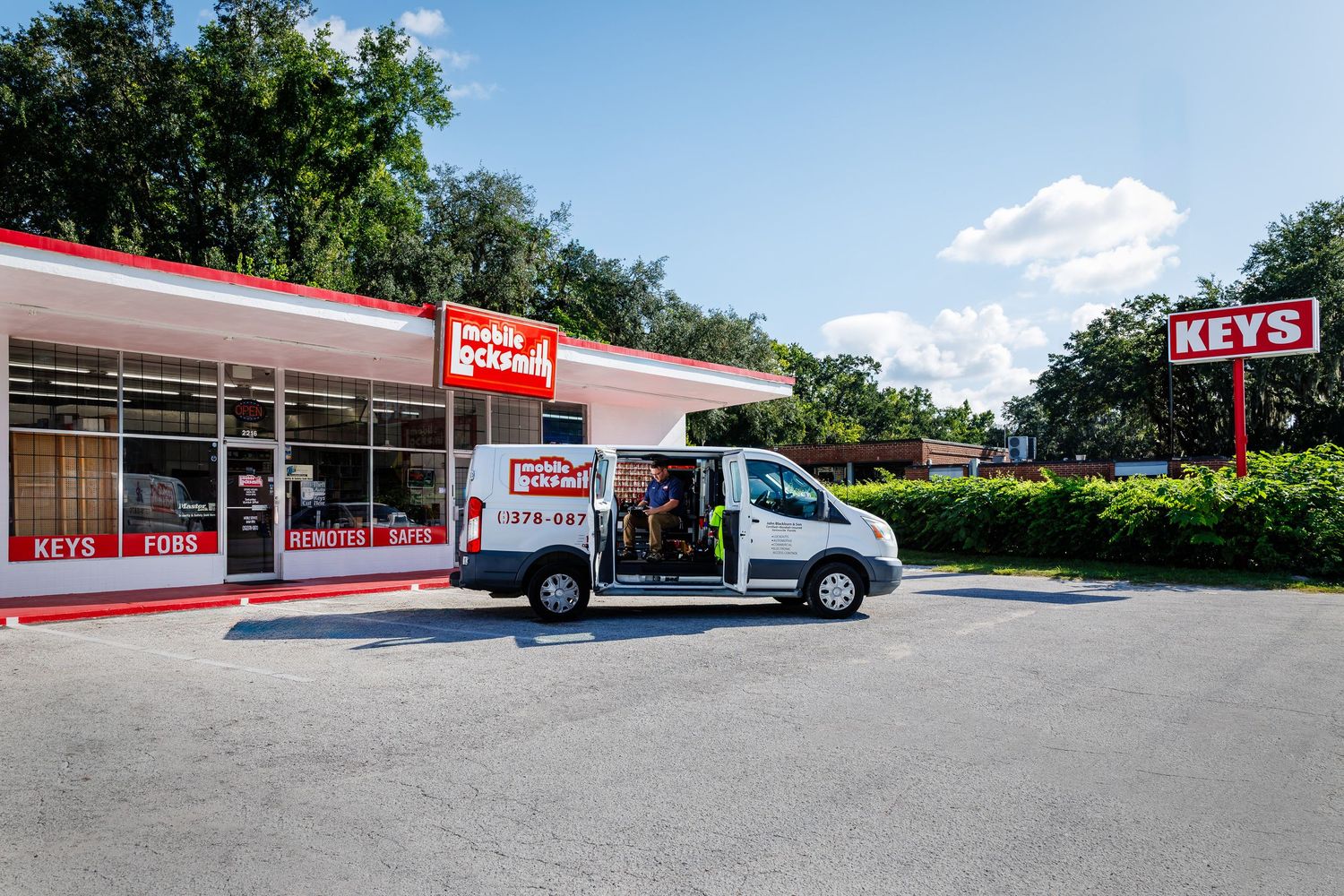 Mobile locksmith with a white van parked in front of a white building with red trim.
