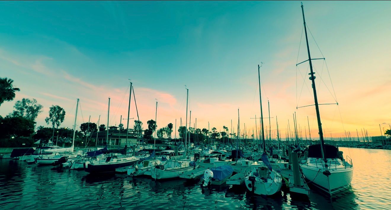 Sailboats docked at a marina during a vibrant sunset with colorful sky reflections on calm water.