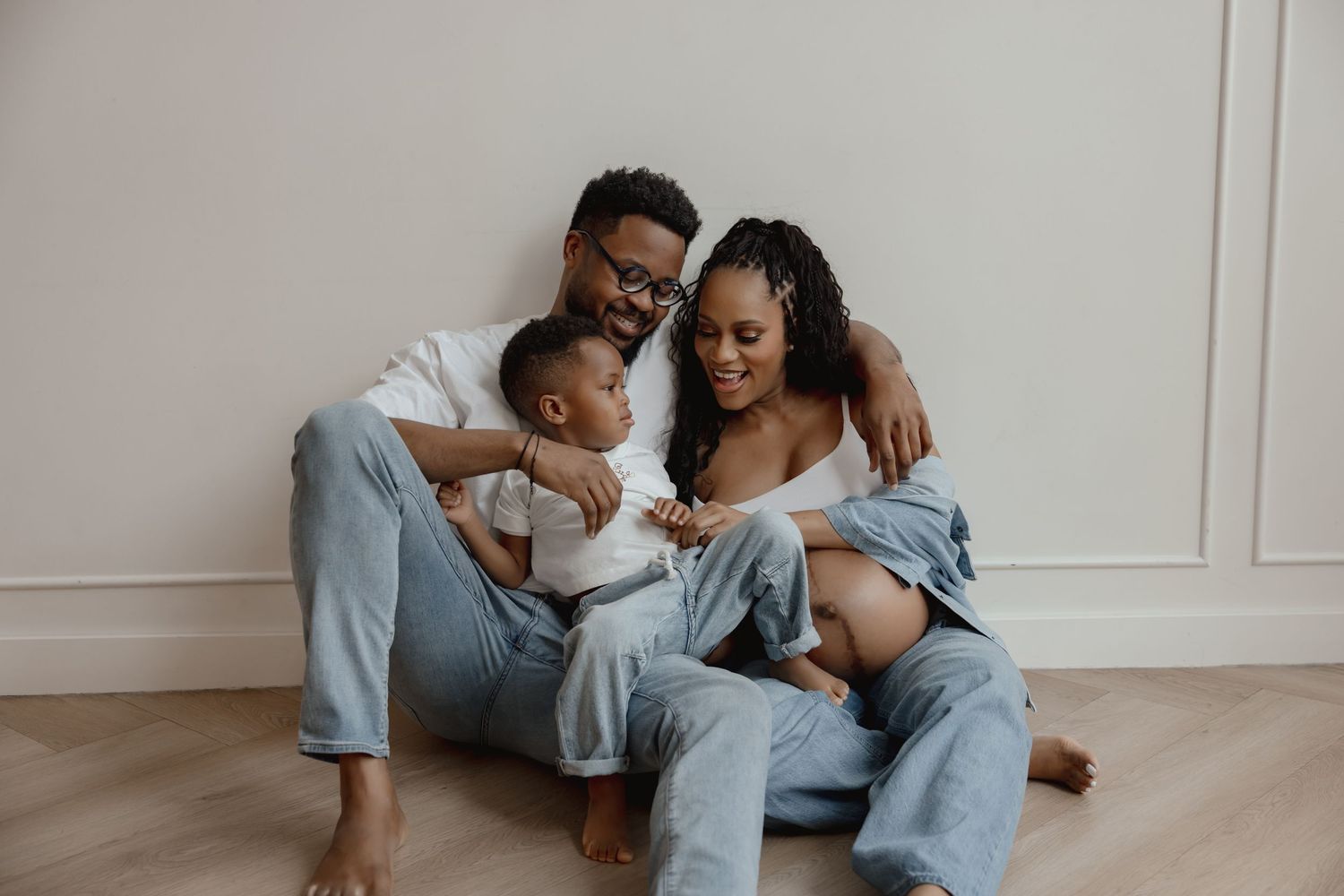 A young Black family sits together in a studio setting during a candid moment for their maternity photoshoot