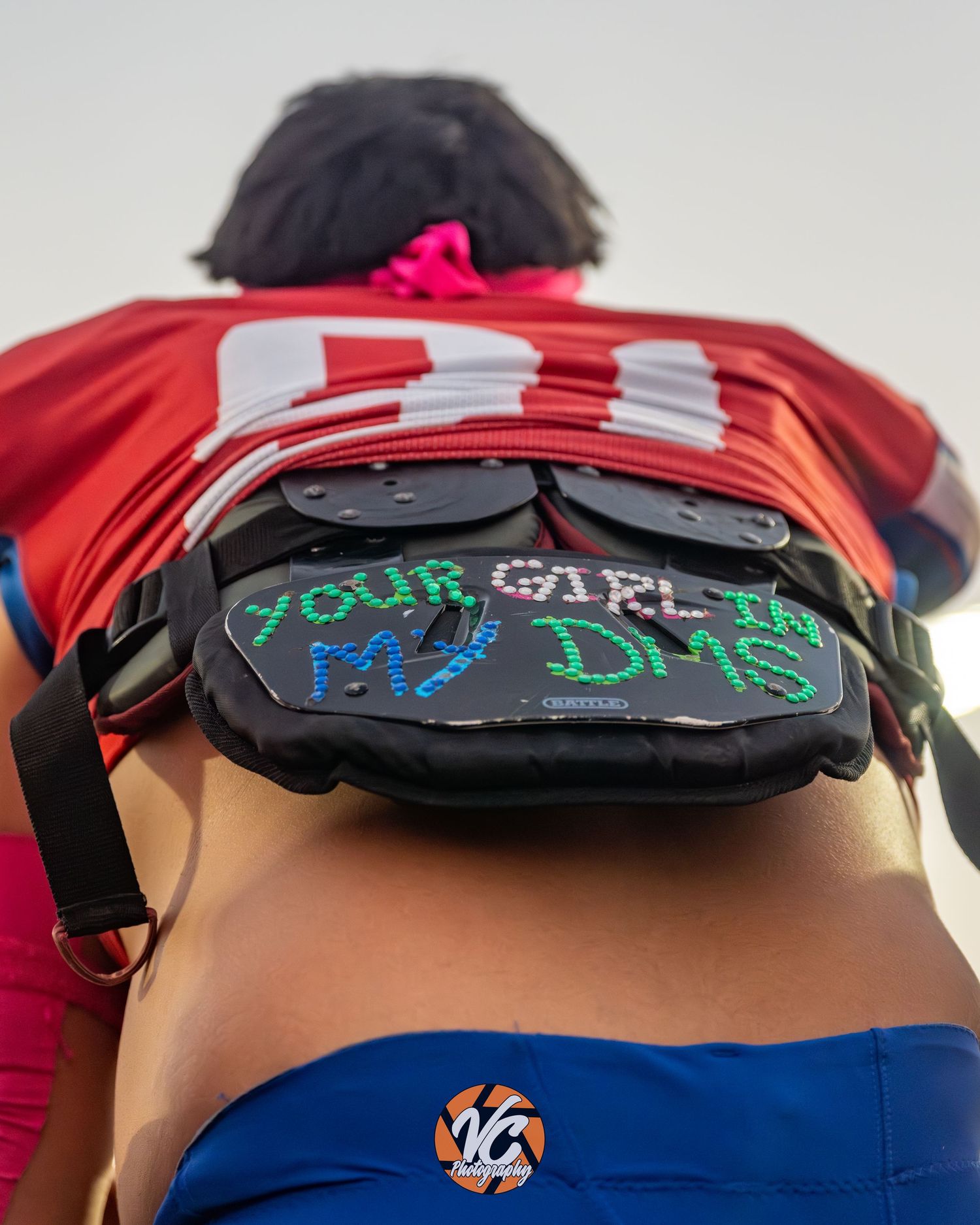 Person wearing red jersey with LED fanny pack displaying text, blue shorts with VC logo, at outdoor event.